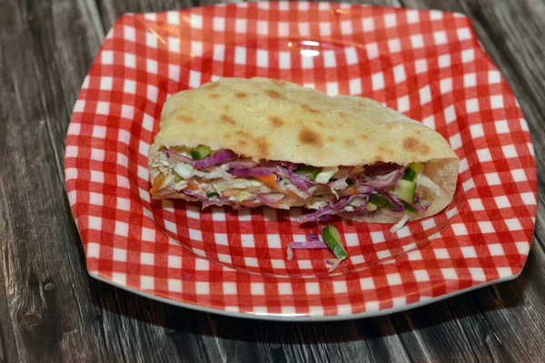 Traditional Egyptian fried potatoes fingers sandwich with slices of red cabbage, kabocha squash, cucumber, carrot and sesame tahini, selective focus of flat bread filled with Potato isolated on wood