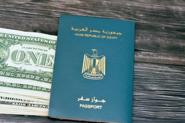 Egyptian passport with American dollars of 1 $ one United states money banknotes isolated on wooden background, Arab republic of Egypt's passport with the republican golden eagle and American money