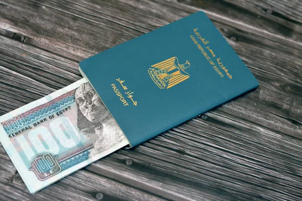 Egyptian passport with 100 EGP LE one hundred Egyptian pounds money banknotes isolated on wooden background, Arab republic of Egypt's passport with the republican golden eagle and Egypt money