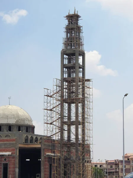 A new mosque under construction against the sunny blue sky with the mosque minaret surrounded with wood scaffold and the dome under construction, selective focus of a new masjid mosque