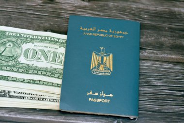 Egyptian passport with American dollars of 1 $ one United states money banknotes isolated on wooden background, Arab republic of Egypt's passport with the republican golden eagle and American money