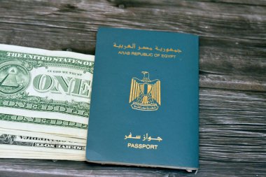 Egyptian passport with American dollars of 1 $ one United states money banknotes isolated on wooden background, Arab republic of Egypt's passport with the republican golden eagle and American money