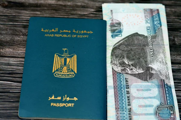 Egyptian passport with 100 EGP LE one hundred Egyptian pounds money banknotes isolated on wooden background, Arab republic of Egypt's passport with the republican golden eagle and Egypt money