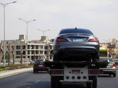 Cairo, Egypt, August 25 2022: A tow recovery transporter hydraulic flatbed truck moving Mercedes Benz CLA 180 car moving in the street, selective focus