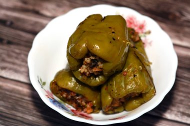 A plate of filled bell peppers stuffed Egyptian mahshi and filled with white rice, onion, parsley, dill and coriander, selective focus of Arabic Egyptian traditional cuisine of Mahshy isolated on wood