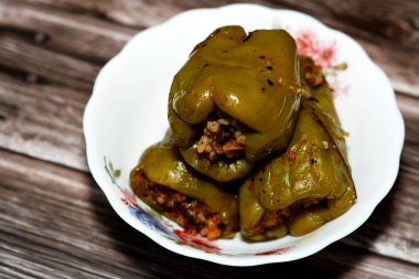 A plate of filled bell peppers stuffed Egyptian mahshi and filled with white rice, onion, parsley, dill and coriander, selective focus of Arabic Egyptian traditional cuisine of Mahshy isolated on wood