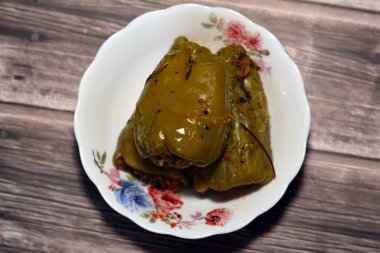 A plate of filled bell peppers stuffed Egyptian mahshi and filled with white rice, onion, parsley, dill and coriander, selective focus of Arabic Egyptian traditional cuisine of Mahshy isolated on wood