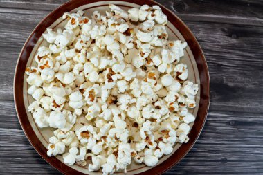 Bir tabak patlamış mısır, patlamış mısır ya da patlamış mısır da denir. Tahta bir arka planda ısıtıldığında genleşen ve şişen mısır çekirdeğinin çeşitliliği seçici bir odak noktasıdır.