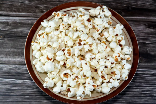 A plate of Popcorn and also called popped corn, popcorns or pop-corn, variety of corn kernel that expands and puffs up when heated isolated on a wooden background, selective focus