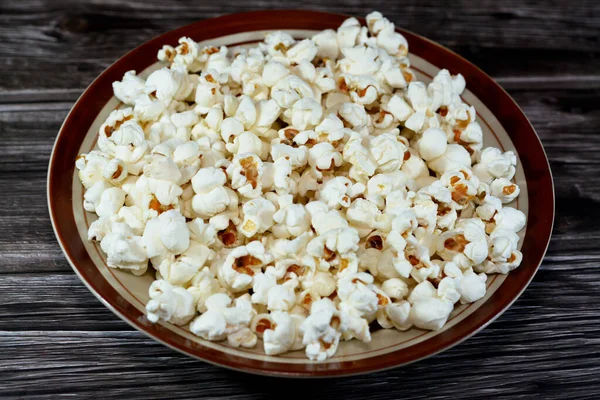 A plate of Popcorn and also called popped corn, popcorns or pop-corn, variety of corn kernel that expands and puffs up when heated isolated on a wooden background, selective focus