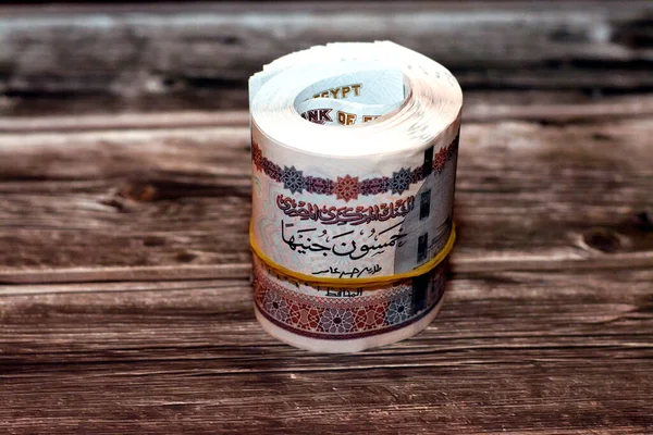 Egypt money roll pounds isolated on wooden background, 50 LE fifty Egyptian pounds cash money bills rolled up with rubber bands with a image of Abu Hurayba Mosque, temple of Edfu and winged scarab