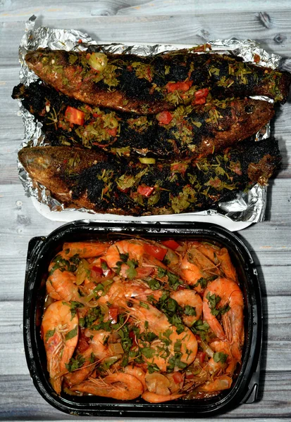 Seafood cuisine of Boiled shrimps mixed garlic, lemon, parsley, pepper, onion and tomato and Charcoal grilled barbecued mullet fish with parsley and tomato isolated on wooden background