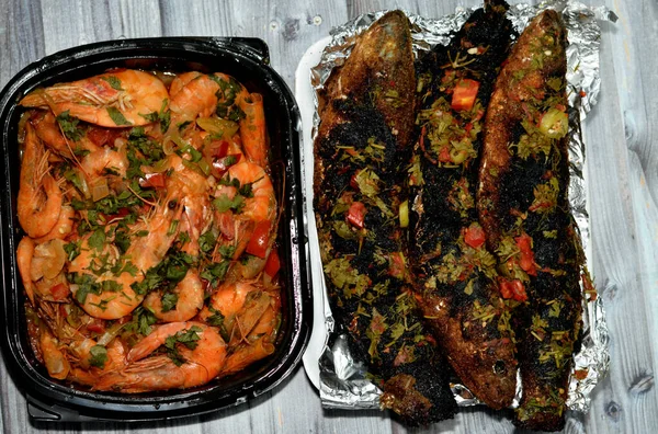 Seafood cuisine of Boiled shrimps mixed garlic, lemon, parsley, pepper, onion and tomato and Charcoal grilled barbecued mullet fish with parsley and tomato isolated on wooden background