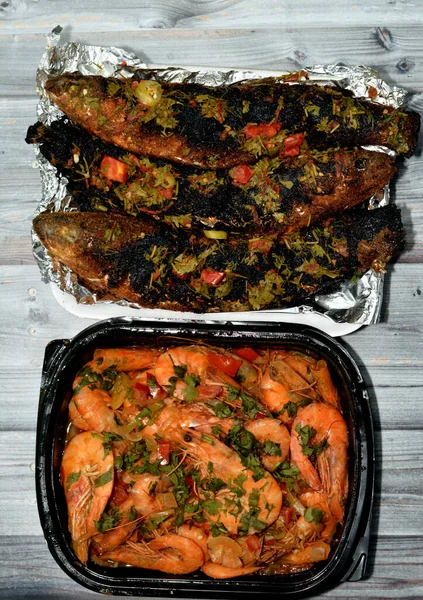 Seafood cuisine of Boiled shrimps mixed garlic, lemon, parsley, pepper, onion and tomato and Charcoal grilled barbecued mullet fish with parsley and tomato isolated on wooden background