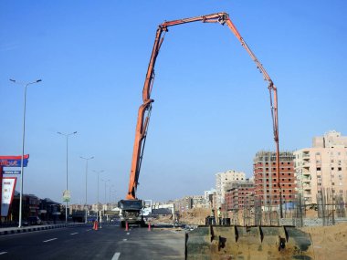 Kahire, Mısır, 3 Ekim 2022: Yolun kenarına kamyon monte edilmiş beton bir patlama pompası, yeni inşaat alanındaki beton kamyonun seçici odak noktası olan yeni bir binaya beton dökülüyor