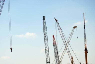 Farklı ağır nesnelerin verimli ve kullanışlı kaldırma ve taşınmasını sağlayan bir fabrikanın inşaat sahasındaki çeşitli mobil telli vinçler, yukarıdaki vinçlerin seçici odak noktası