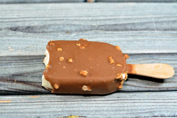 茶色のミルクチョコレートとローストアーモンドの分離割れで豊かなバニラ風味のアイスクリーム バニラアイススティックコーティングされ ナッツとダークチョコレートの層で覆われ 選択的な焦点 — ストック写真
