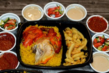 Uzun basmati pilavı ve patates kızartmasıyla tavuklu mandi kabsa, domates sosu, yeşil salata ve tahini, Yemen usulü baharatlı ve soslu Mandi tavuğu tarifinin seçici odağı.