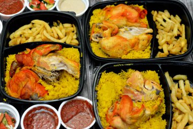 Uzun basmati pilavı ve patates kızartmasıyla tavuklu mandi kabsa, domates sosu, yeşil salata ve tahini, Yemen usulü baharatlı ve soslu Mandi tavuğu tarifinin seçici odağı.