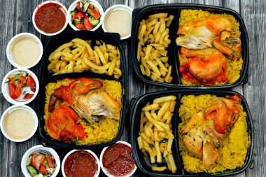 Uzun basmati pilavı ve patates kızartmasıyla tavuklu mandi kabsa, domates sosu, yeşil salata ve tahini, Yemen usulü baharatlı ve soslu Mandi tavuğu tarifinin seçici odağı.