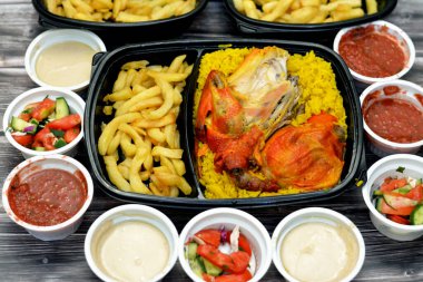 Uzun basmati pilavı ve patates kızartmasıyla tavuklu mandi kabsa, domates sosu, yeşil salata ve tahini, Yemen usulü baharatlı ve soslu Mandi tavuğu tarifinin seçici odağı.