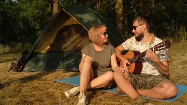 Homme et femme chantent la chanson avec guitare assis à la tente.Touristes est en voyage de camping. — Video