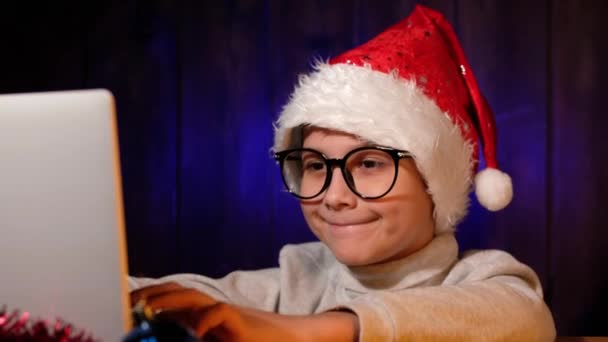 Niño con un sombrero rojo escribe carta a Santa Claus en el ordenador portátil en Nochebuena. — Vídeos de Stock