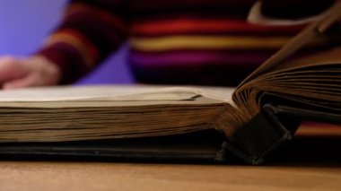 Yaşlı bir kadın aile albümüne bakıyor. Masasında eski fotoğraflar var..