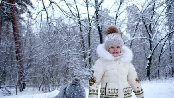 Маленькі діти кидають сніг гуляти в лісі. Щасливий хлопчик і дівчинка насолоджуються зимою . — стокове відео