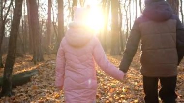 Küçük oğlan ve kız sonbahar ormanlarında el ele yürürler. Çocuklar parkta yürüyor..