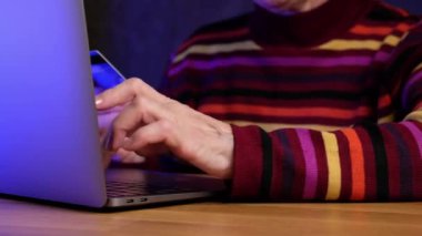 Modern emekli kadın, dizüstü bilgisayarındaki kredi kartıyla online alışveriş yapıyor..
