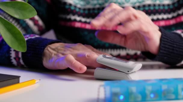 Mujer mayor se pone oxímetro digital en la punta de los dedos para medir la cantidad de oxígeno en la sangre y los niveles de pulso en casa. — Vídeo de stock