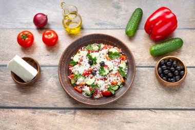 Ahşap arka planda en tepeden gelen malzemelerle yapılan Shopska salatası: biber, salatalık, zeytin, zeytin yağı, feta peyniri, domates, soğan, maydanoz. Yatay düz görünüm.