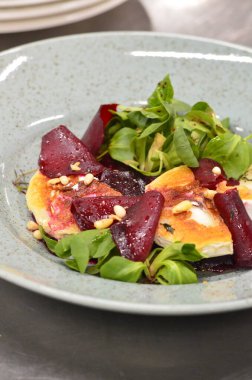 Kavrulmuş keçi peynirli pancar kökü salatası ve kırsal bir restoranın arka planındaki bir restorandaki ahşap masaya dayanan otlar.