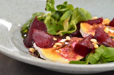 Kavrulmuş keçi peynirli pancar kökü salatası ve kırsal bir restoranın arka planındaki bir restorandaki ahşap masaya dayanan otlar.