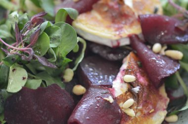 Kavrulmuş keçi peynirli pancar kökü salatası ve kırsal bir restoranın arka planındaki bir restorandaki ahşap masaya dayanan otlar.