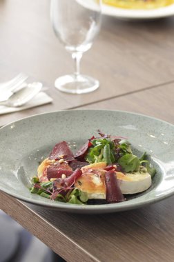 Kavrulmuş keçi peynirli pancar kökü salatası ve kırsal bir restoranın arka planındaki bir restorandaki ahşap masaya dayanan otlar.