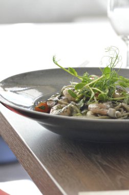 Karides, kiraz domatesli taze sepia makarna, ahşap masa ve kırsal tabak üzerinde restoran arka planı, basit modern yemek menüsü.