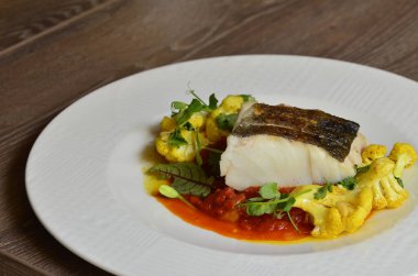 Kırmızı biber soslu morina balığı bifteği ve körili karnabahar, taze otlarla süslenmiş, masadaki bir restoranda servis edilen Akdeniz yemeği.