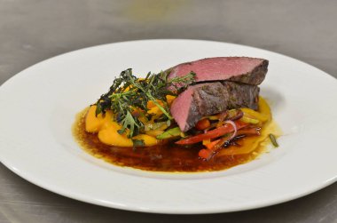 Orta boy biftek fileto, meze, sebze, restoranda beyaz tabakta servis edilen yemekler.