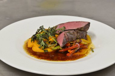 Orta boy biftek fileto, meze, sebze, restoranda beyaz tabakta servis edilen yemekler.