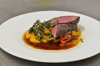 Orta boy biftek fileto, meze, sebze, restoranda beyaz tabakta servis edilen yemekler.