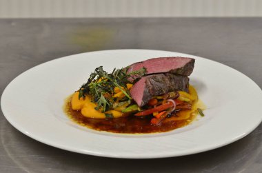 Orta boy biftek fileto, meze, sebze, restoranda beyaz tabakta servis edilen yemekler.