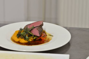 Orta boy biftek fileto, meze, sebze, restoranda beyaz tabakta servis edilen yemekler.