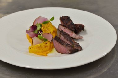 Orta boy biftek fileto, meze, sebze, restoranda beyaz tabakta servis edilen yemekler.