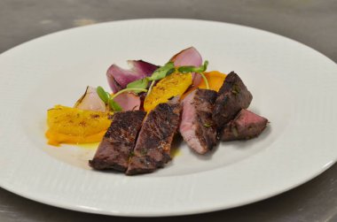 Orta boy biftek fileto, meze, sebze, restoranda beyaz tabakta servis edilen yemekler.