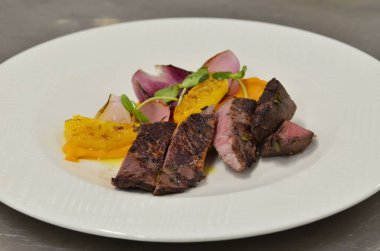 Orta boy biftek fileto, meze, sebze, restoranda beyaz tabakta servis edilen yemekler.