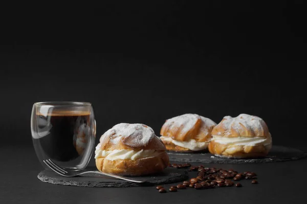 在黑色的背景上 在黑色的盘子里放着带有奶油和糖粉的月桂 一杯咖啡和咖啡豆完成了这张照片 — 图库照片