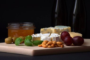 Dilimlenmiş peynirler, bal, fındık, zeytin, fesleğen yaprakları ahşap bir tahtaya istiflenmiş.