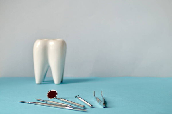 on the table in front of a beautiful white tooth lie the dentist\\\'s dental instruments. The picture is horizontal